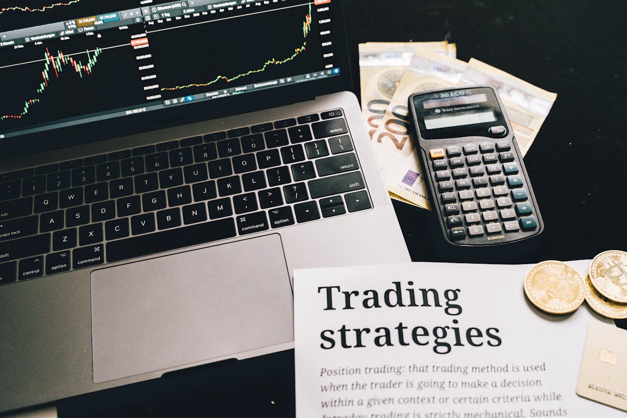 Close-up image of a trading setup with a laptop, calculator, and financial documents, ideal for finance and stock market themes.